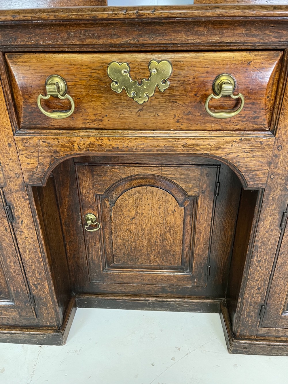 A large dark oak dresser featuring a multi-tiered open plate rack top above a wide base with drawers and panelled cupboard doors. View II