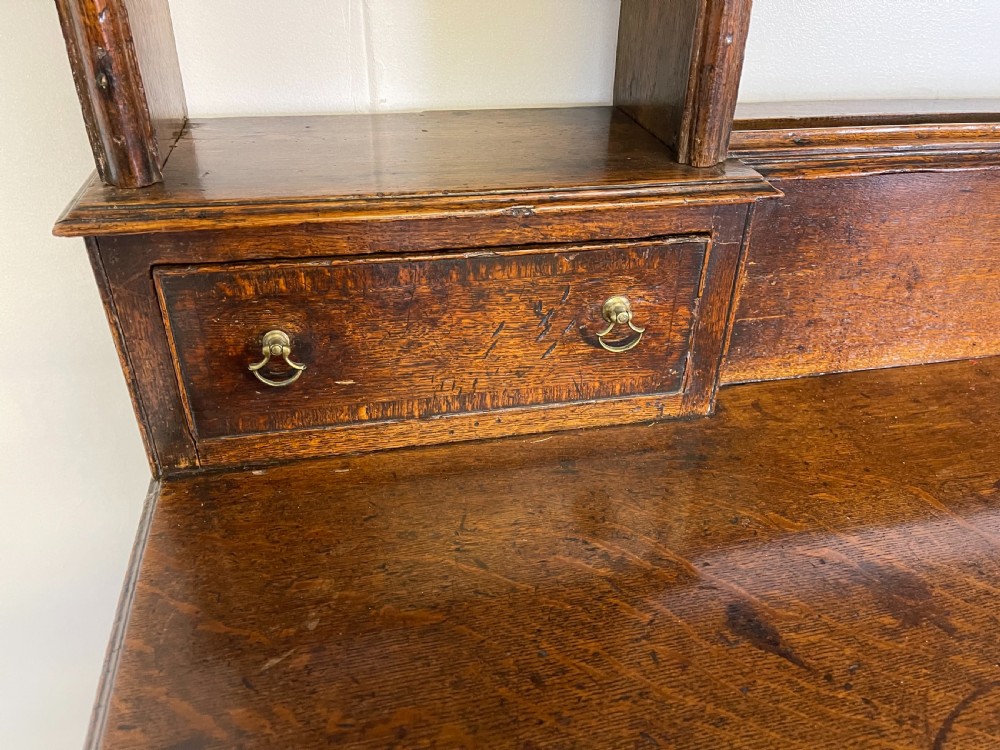 A large dark oak dresser featuring a multi-tiered open plate rack top above a wide base with drawers and panelled cupboard doors. View IV