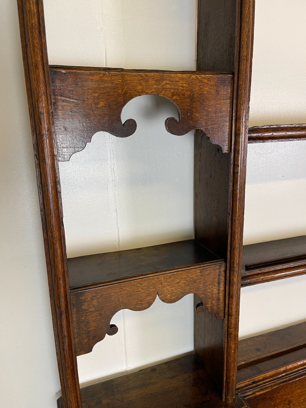A large dark oak dresser featuring a multi-tiered open plate rack top above a wide base with drawers and panelled cupboard doors. View VII