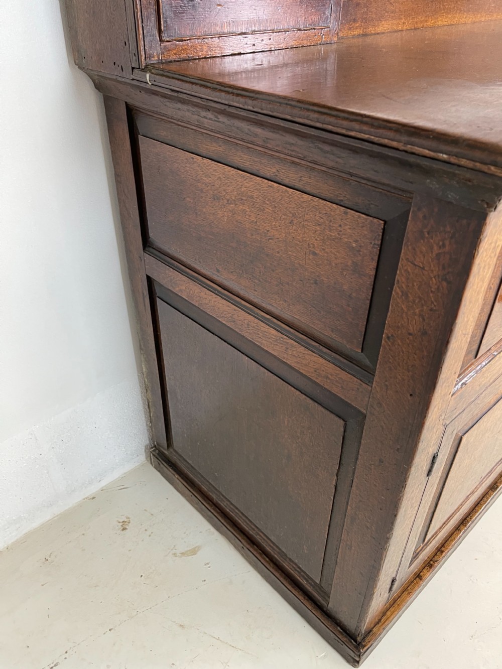 A large dark oak dresser featuring a multi-tiered open plate rack top above a wide base with drawers and panelled cupboard doors. View X