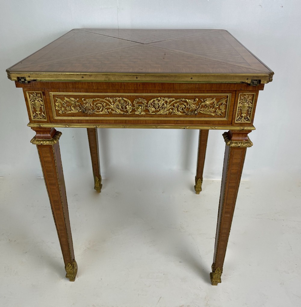 A square French Louis XVI style parquetry envelope card table featuring detailed gilt-bronze mounts and tapered legs.