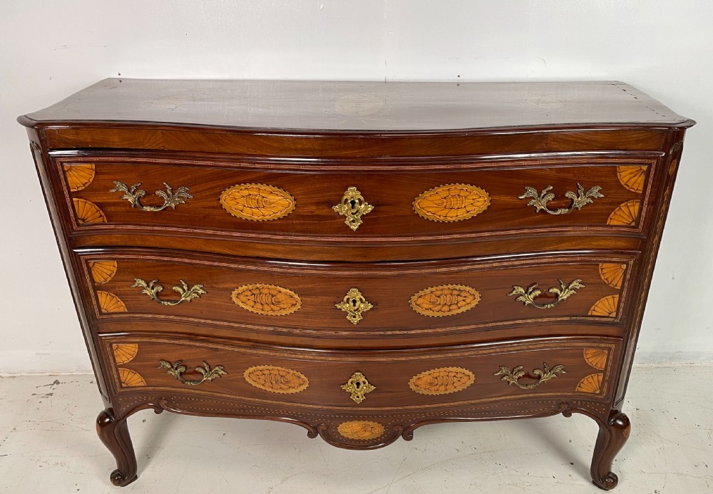 An 18th-century French walnut commode featuring three drawers with elaborate fruitwood marquetry inlays, cast brass escutcheons, and curved cabriole legs.