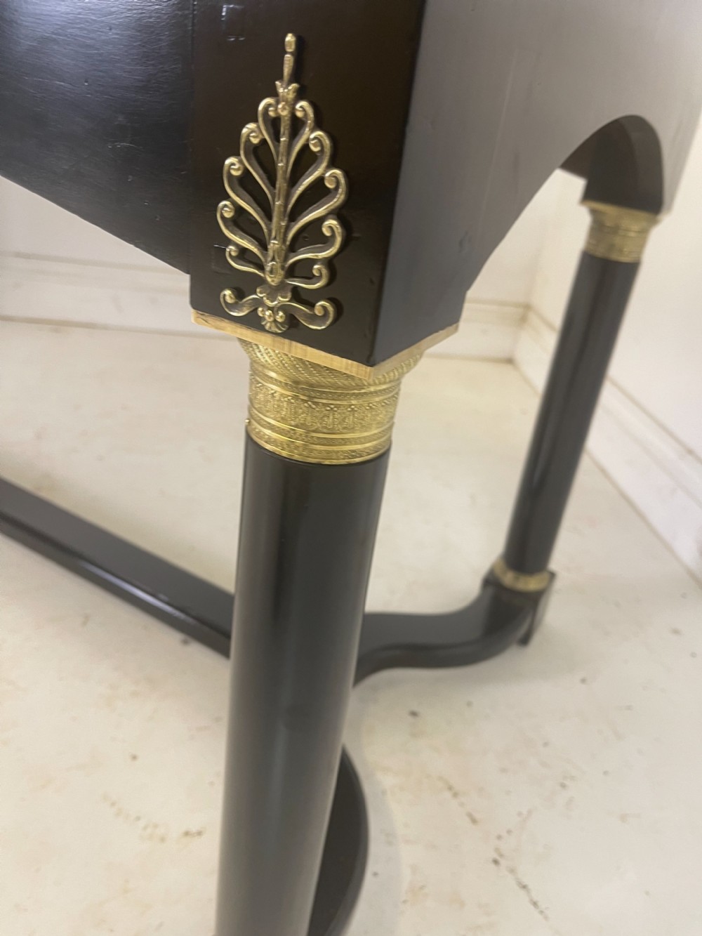 A black ebonised Empire style writing desk featuring a green leather inset top, two frieze drawers with brass knobs, ornate brass mounts, and cylindrical legs connected by a lower stretcher. View VI