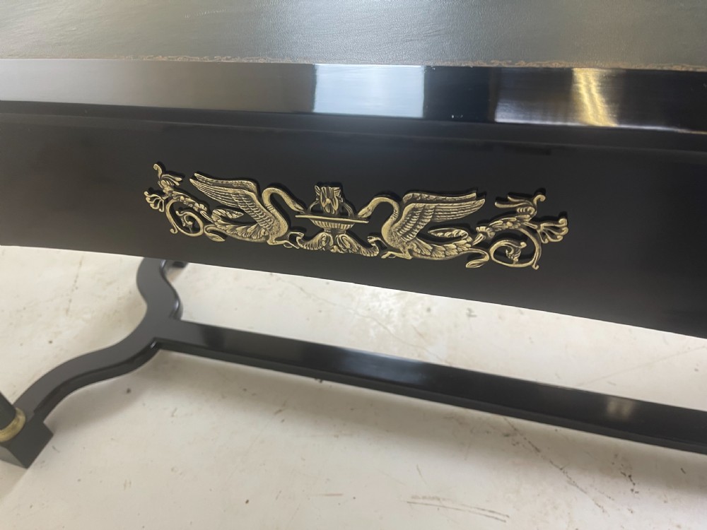 A black ebonised Empire style writing desk featuring a green leather inset top, two frieze drawers with brass knobs, ornate brass mounts, and cylindrical legs connected by a lower stretcher. View VIII