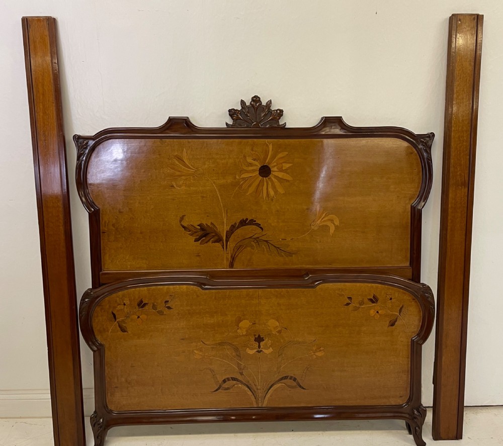 An Art Nouveau wooden bed frame featuring floral marquetry inlay on the headboard and footboard with carved organic scrollwork.