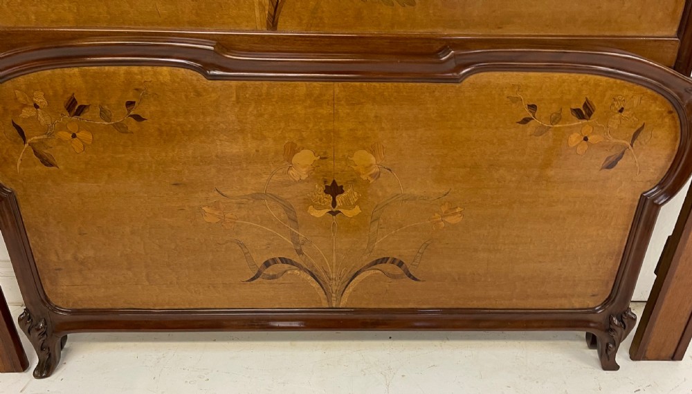 An Art Nouveau wooden bed frame featuring floral marquetry inlay on the headboard and footboard with carved organic scrollwork. View II