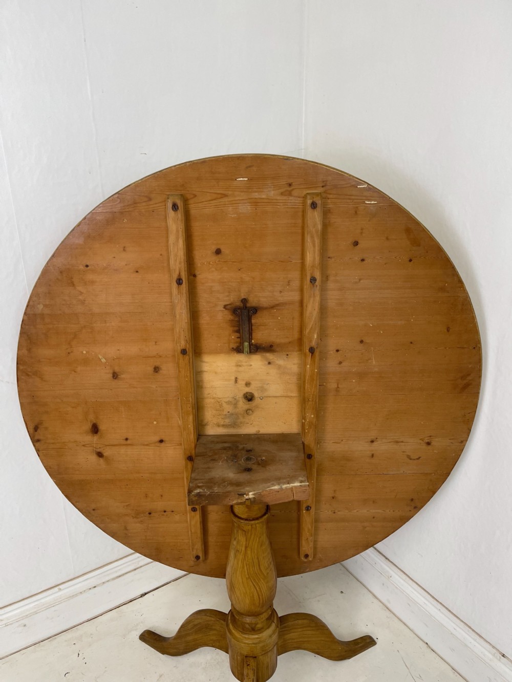 A circular pine tilt-top table presented in its raised vertical position showing its natural timber grain and tripod base. View III