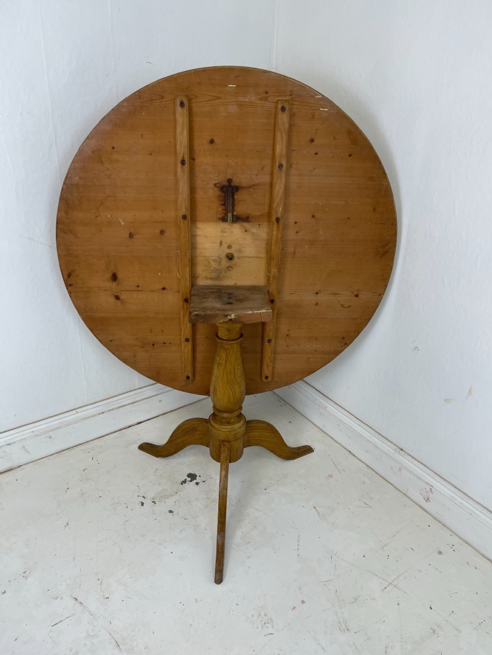 A circular pine tilt-top table presented in its raised vertical position showing its natural timber grain and tripod base. View V