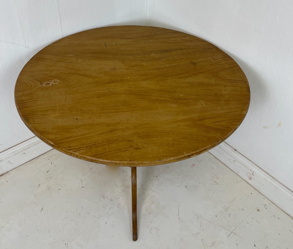 A circular pine tilt-top table presented in its raised vertical position showing its natural timber grain and tripod base. View VI