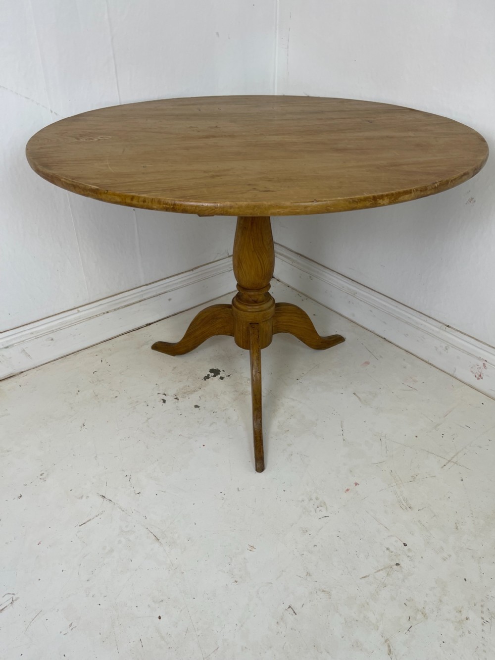 A circular pine tilt-top table presented in its raised vertical position showing its natural timber grain and tripod base. View VII