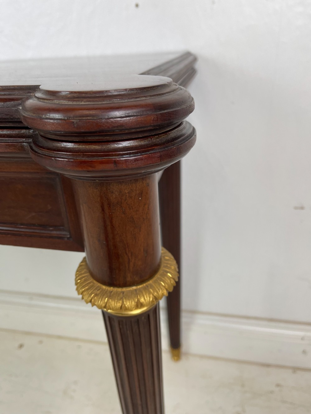 A polished dark mahogany fold-over card table featuring tapered fluted legs topped with gilt bronze acanthus collars. View II