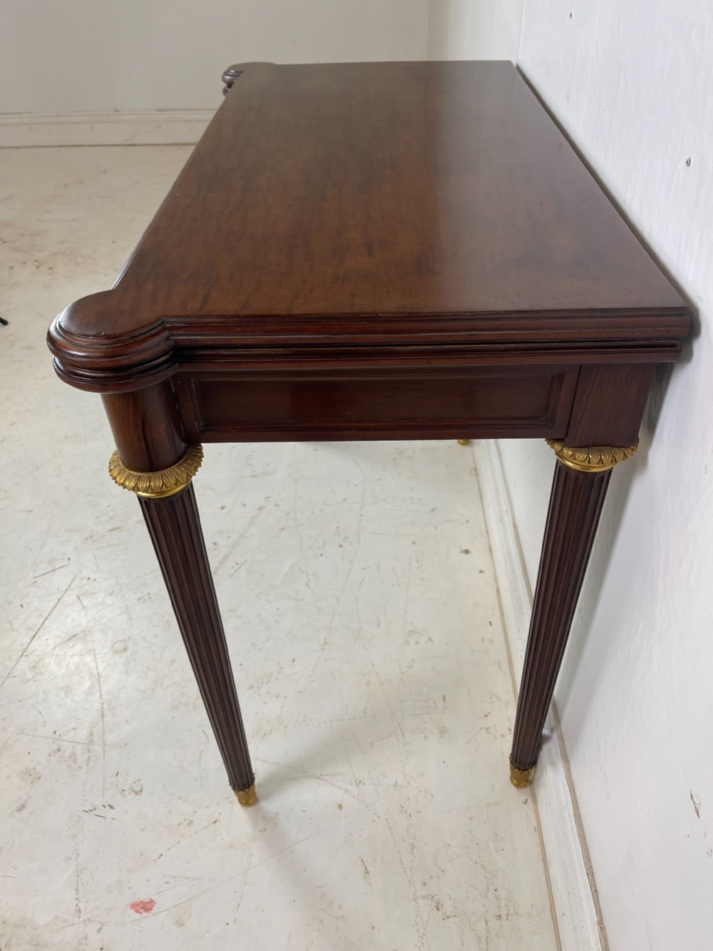 A polished dark mahogany fold-over card table featuring tapered fluted legs topped with gilt bronze acanthus collars. View VI