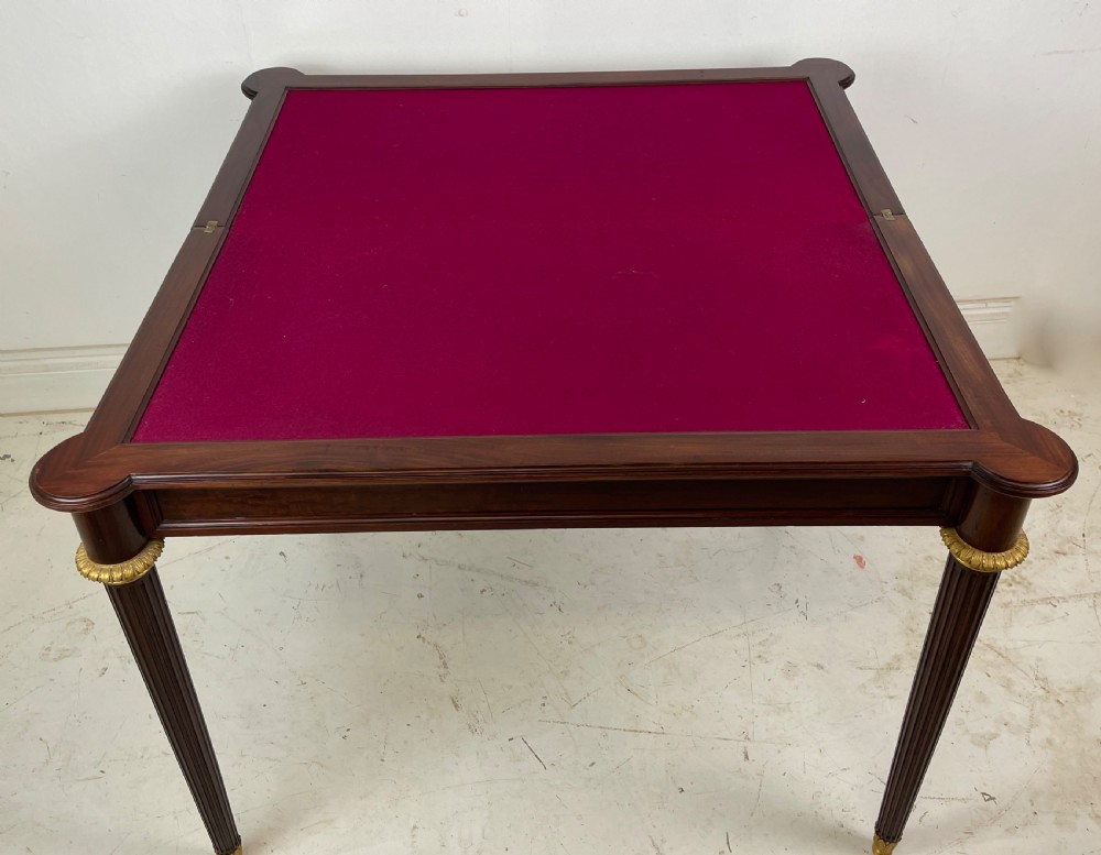 A polished dark mahogany fold-over card table featuring tapered fluted legs topped with gilt bronze acanthus collars. View VIII