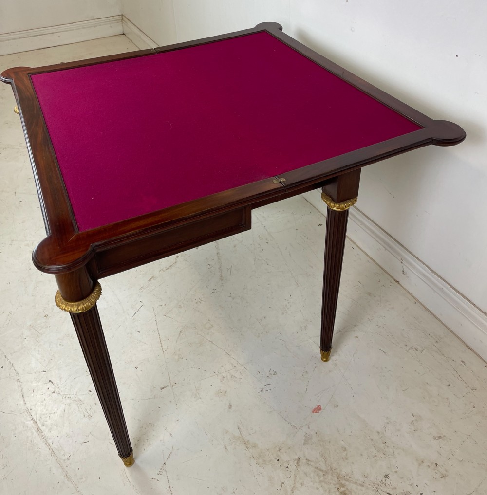 A polished dark mahogany fold-over card table featuring tapered fluted legs topped with gilt bronze acanthus collars. View IX
