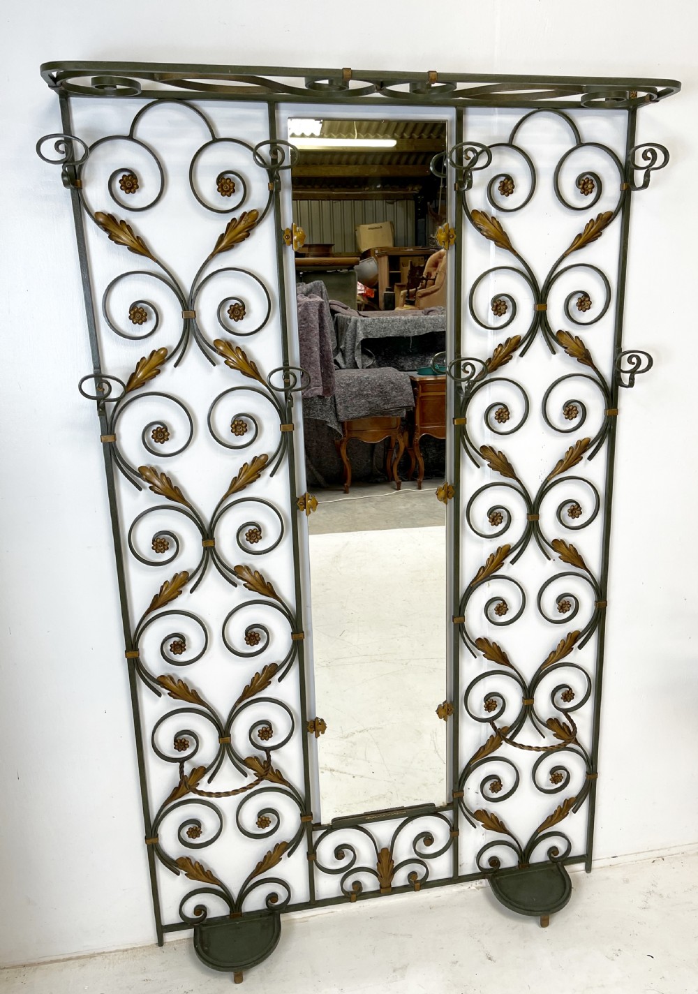 A tall French Art Deco wrought iron hall stand featuring symmetrical scrollwork with gold leaf accents, a central full-length mirror, multiple hooks, and umbrella drip trays.