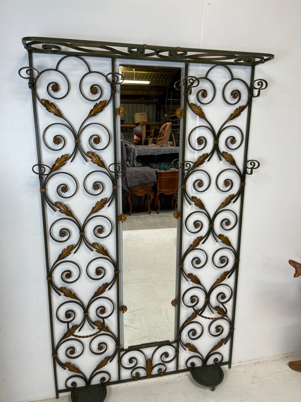 A tall French Art Deco wrought iron hall stand featuring symmetrical scrollwork with gold leaf accents, a central full-length mirror, multiple hooks, and umbrella drip trays. View II
