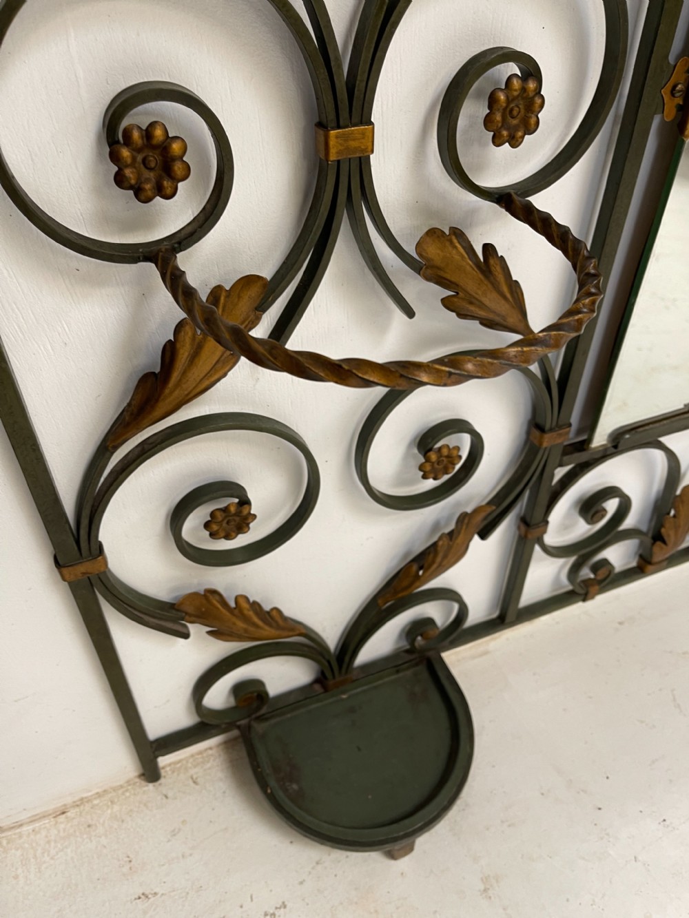 A tall French Art Deco wrought iron hall stand featuring symmetrical scrollwork with gold leaf accents, a central full-length mirror, multiple hooks, and umbrella drip trays. View VI