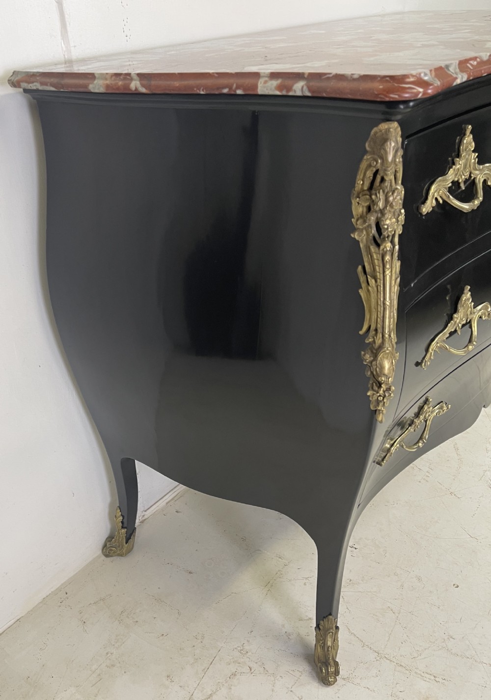 A pair of black ebonised Louis XV style bombee commodes featuring pink marble tops and ornate gilt metal mounts. View II