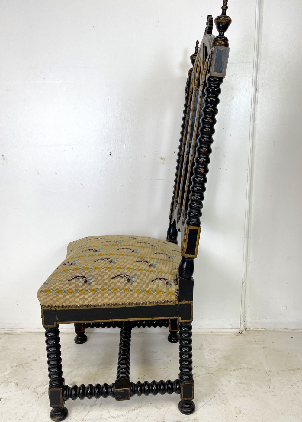 A Victorian Gothic Revival side chair featuring an ebonised frame with lancet arch tracery, bobbin turned legs, and patterned cream upholstery with brass stud details. View VII