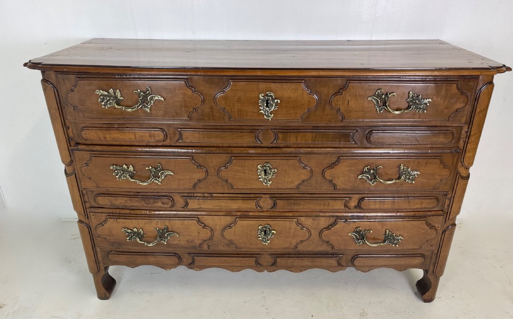 An eighteenth-century French provincial fruitwood commode featuring three wide drawers with moulded panel fronts, ornate brass rococo handles, and short curved legs.