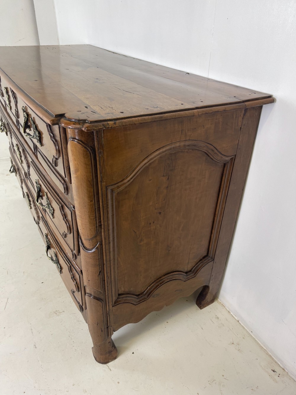 An eighteenth-century French provincial fruitwood commode featuring three wide drawers with moulded panel fronts, ornate brass rococo handles, and short curved legs. View II
