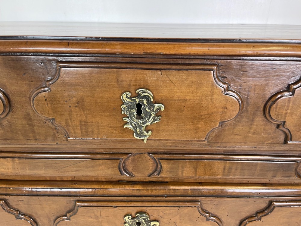 An eighteenth-century French provincial fruitwood commode featuring three wide drawers with moulded panel fronts, ornate brass rococo handles, and short curved legs. View III
