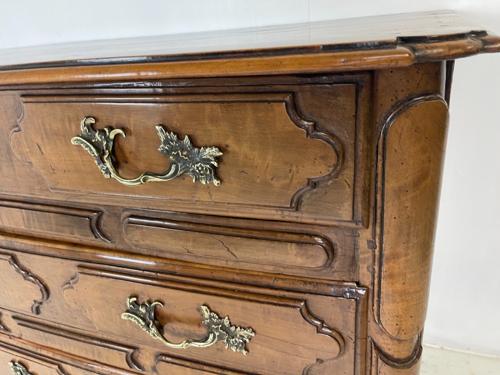 An eighteenth-century French provincial fruitwood commode featuring three wide drawers with moulded panel fronts, ornate brass rococo handles, and short curved legs. View V