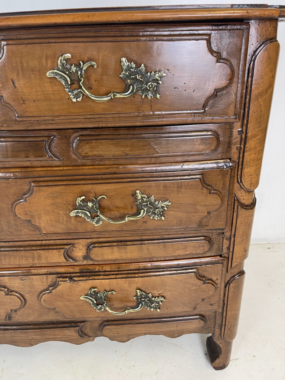 An eighteenth-century French provincial fruitwood commode featuring three wide drawers with moulded panel fronts, ornate brass rococo handles, and short curved legs. View VI