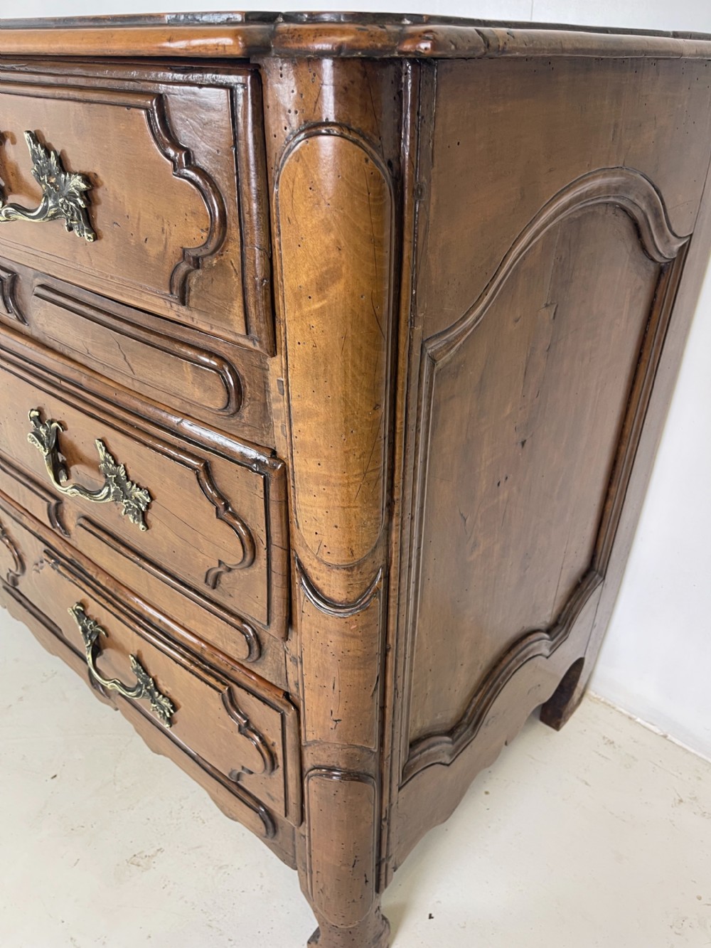 An eighteenth-century French provincial fruitwood commode featuring three wide drawers with moulded panel fronts, ornate brass rococo handles, and short curved legs. View VII