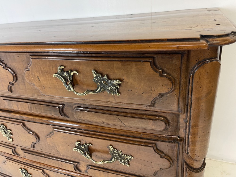 An eighteenth-century French provincial fruitwood commode featuring three wide drawers with moulded panel fronts, ornate brass rococo handles, and short curved legs. View XI