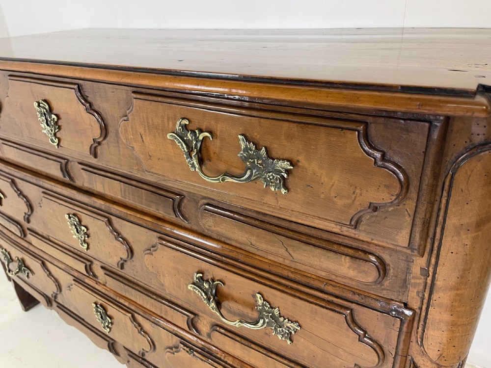 An eighteenth-century French provincial fruitwood commode featuring three wide drawers with moulded panel fronts, ornate brass rococo handles, and short curved legs. View XII