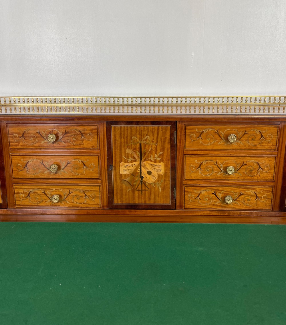 An Edwardian satinwood Carlton House desk with floral marquetry inlay, a green leather writing surface, multiple drawers, and a brass gallery top. View IV