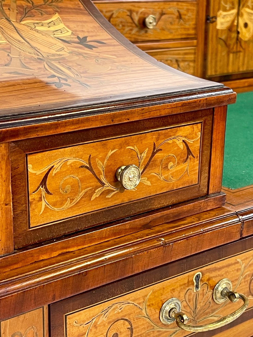An Edwardian satinwood Carlton House desk with floral marquetry inlay, a green leather writing surface, multiple drawers, and a brass gallery top. View VI