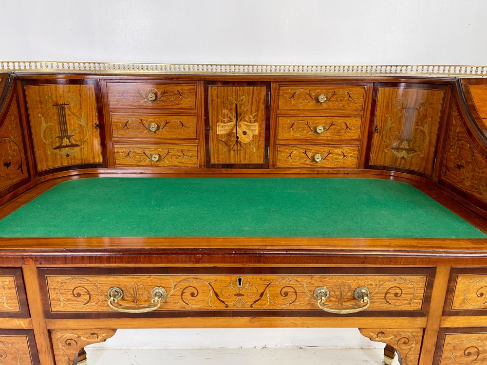 An Edwardian satinwood Carlton House desk with floral marquetry inlay, a green leather writing surface, multiple drawers, and a brass gallery top. View VII