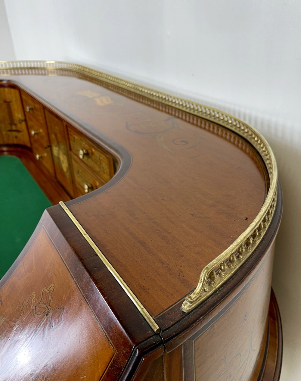 An Edwardian satinwood Carlton House desk with floral marquetry inlay, a green leather writing surface, multiple drawers, and a brass gallery top. View VIII