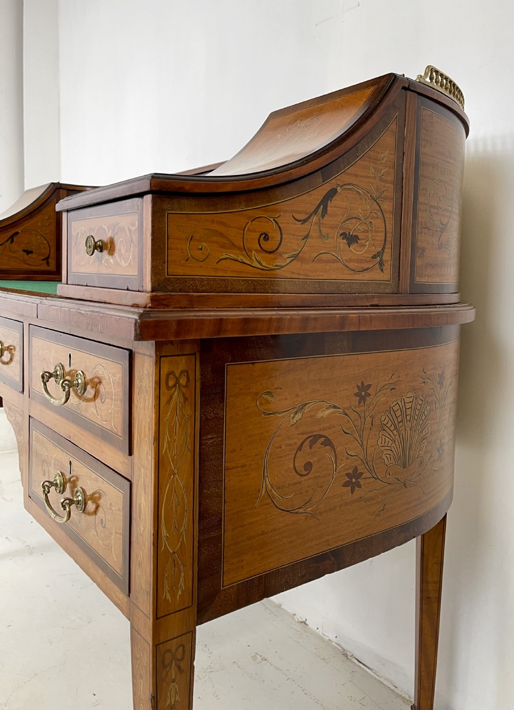 An Edwardian satinwood Carlton House desk with floral marquetry inlay, a green leather writing surface, multiple drawers, and a brass gallery top. View IX