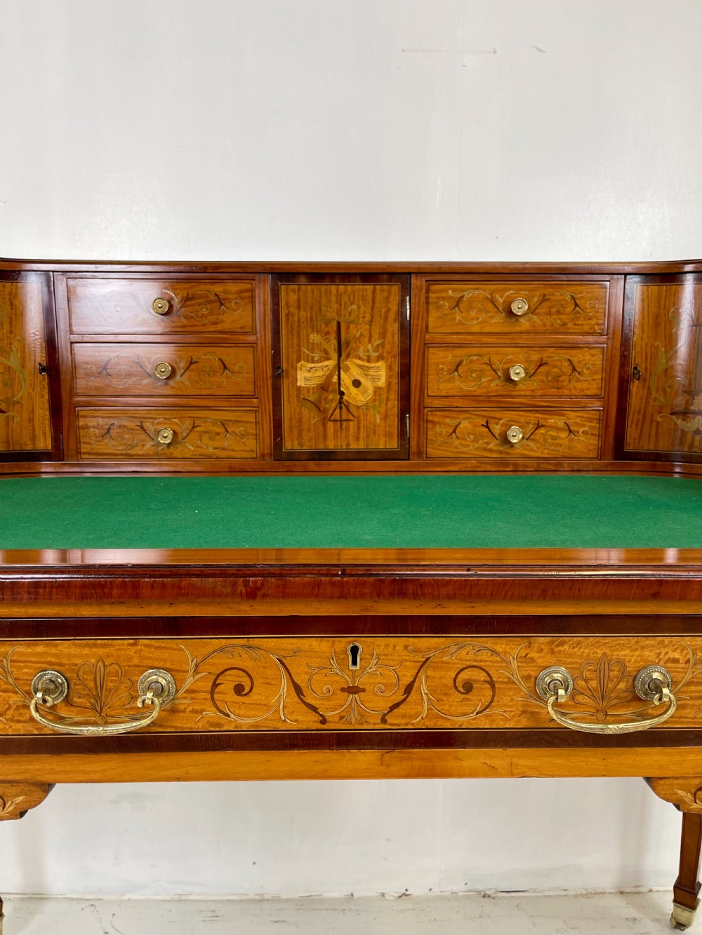 An Edwardian satinwood Carlton House desk with floral marquetry inlay, a green leather writing surface, multiple drawers, and a brass gallery top. View X
