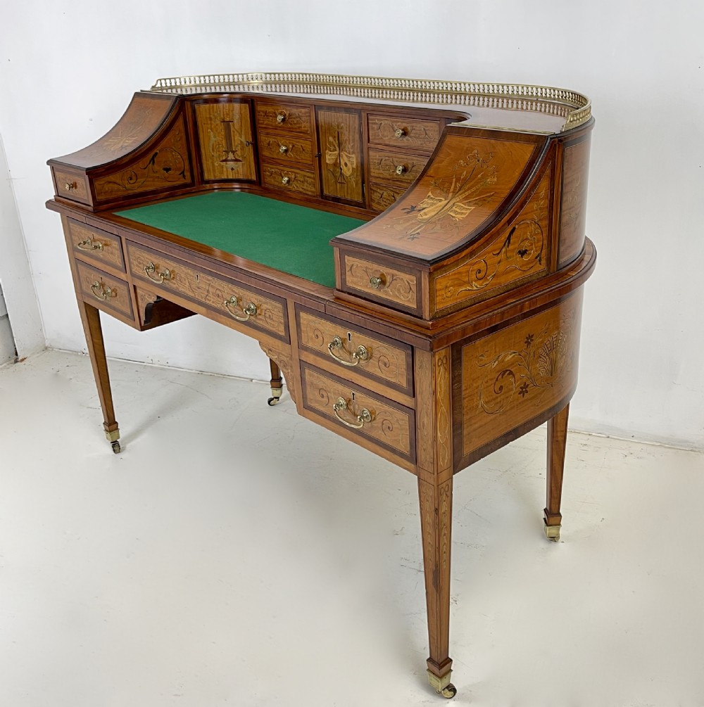 An Edwardian satinwood Carlton House desk with floral marquetry inlay, a green leather writing surface, multiple drawers, and a brass gallery top. View XI