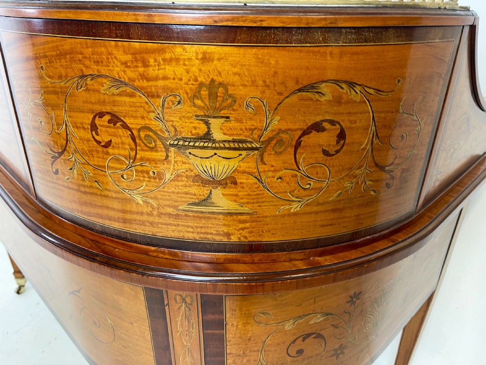 An Edwardian satinwood Carlton House desk with floral marquetry inlay, a green leather writing surface, multiple drawers, and a brass gallery top. View XIII