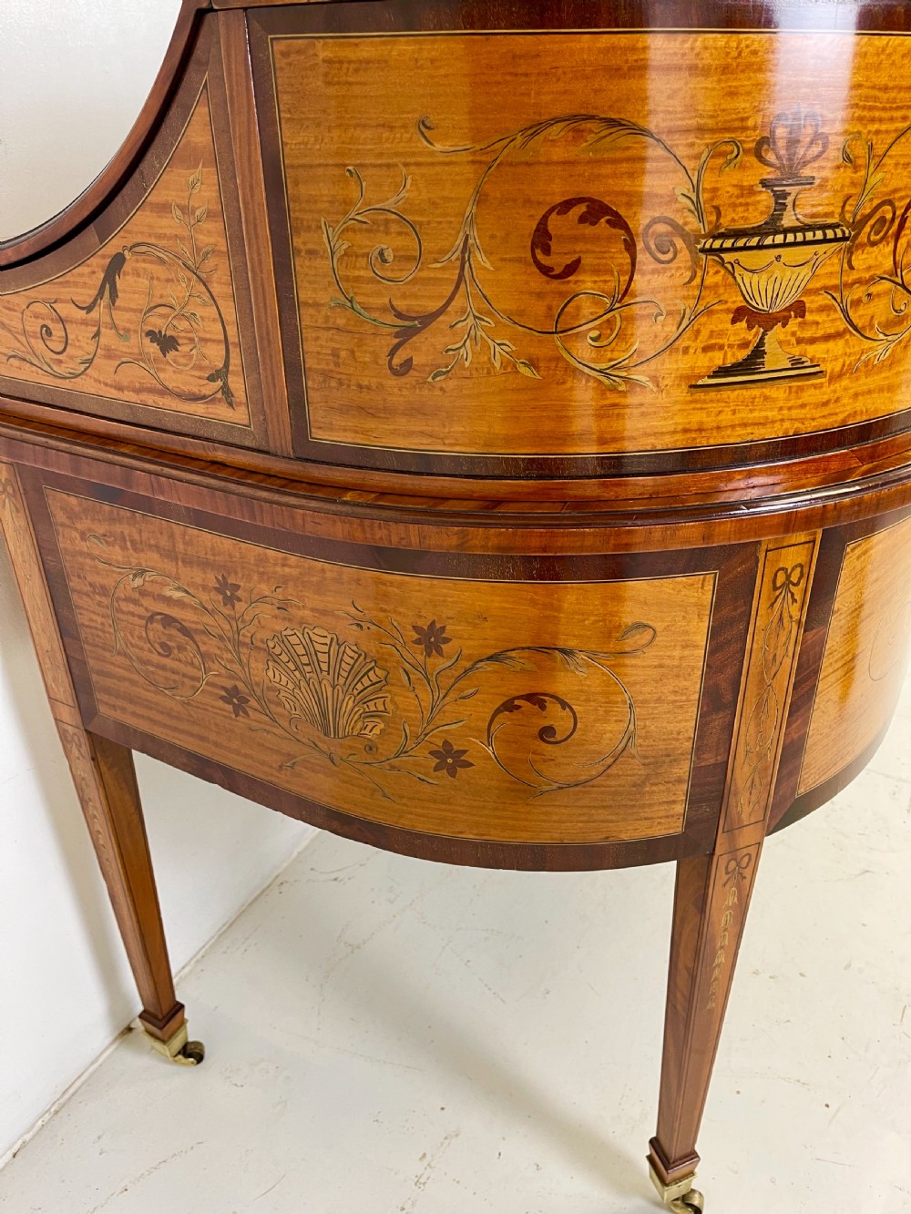 An Edwardian satinwood Carlton House desk with floral marquetry inlay, a green leather writing surface, multiple drawers, and a brass gallery top. View XVI