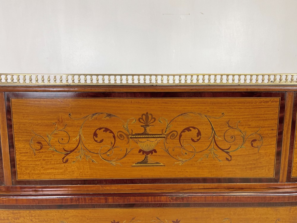 An Edwardian satinwood Carlton House desk with floral marquetry inlay, a green leather writing surface, multiple drawers, and a brass gallery top. View XVII