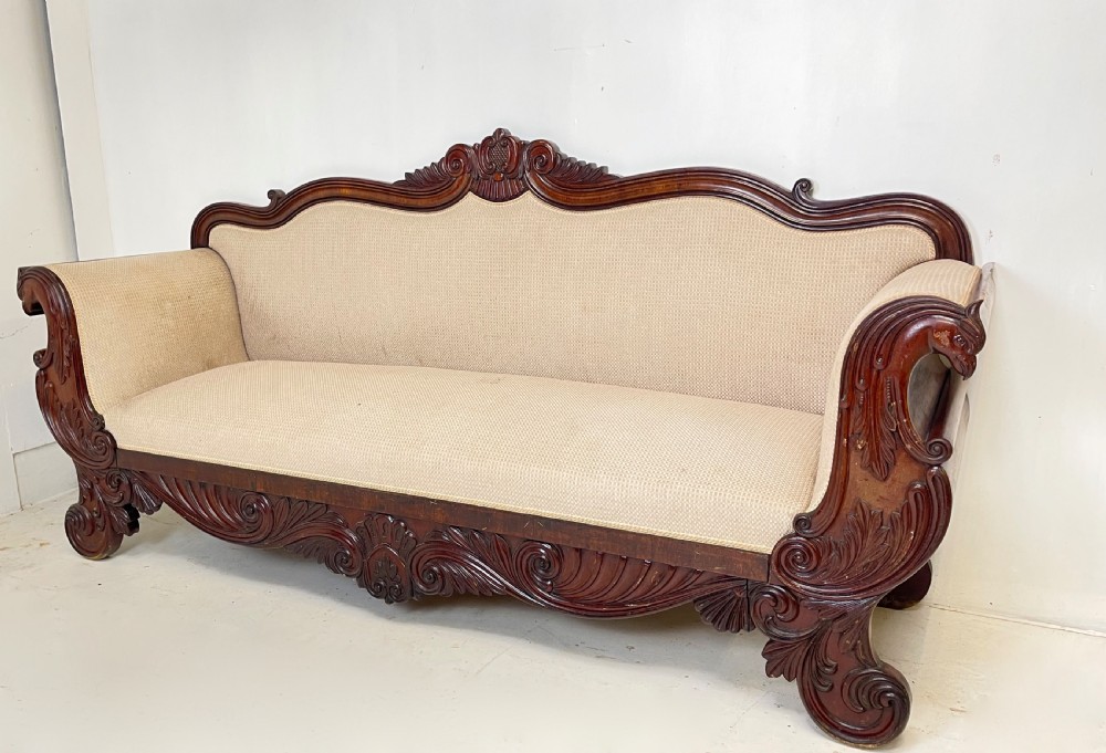A large antique mahogany sofa featuring intricately hand-carved acanthus scrollwork along the apron and arms, upholstered in a light cream textured fabric. View V