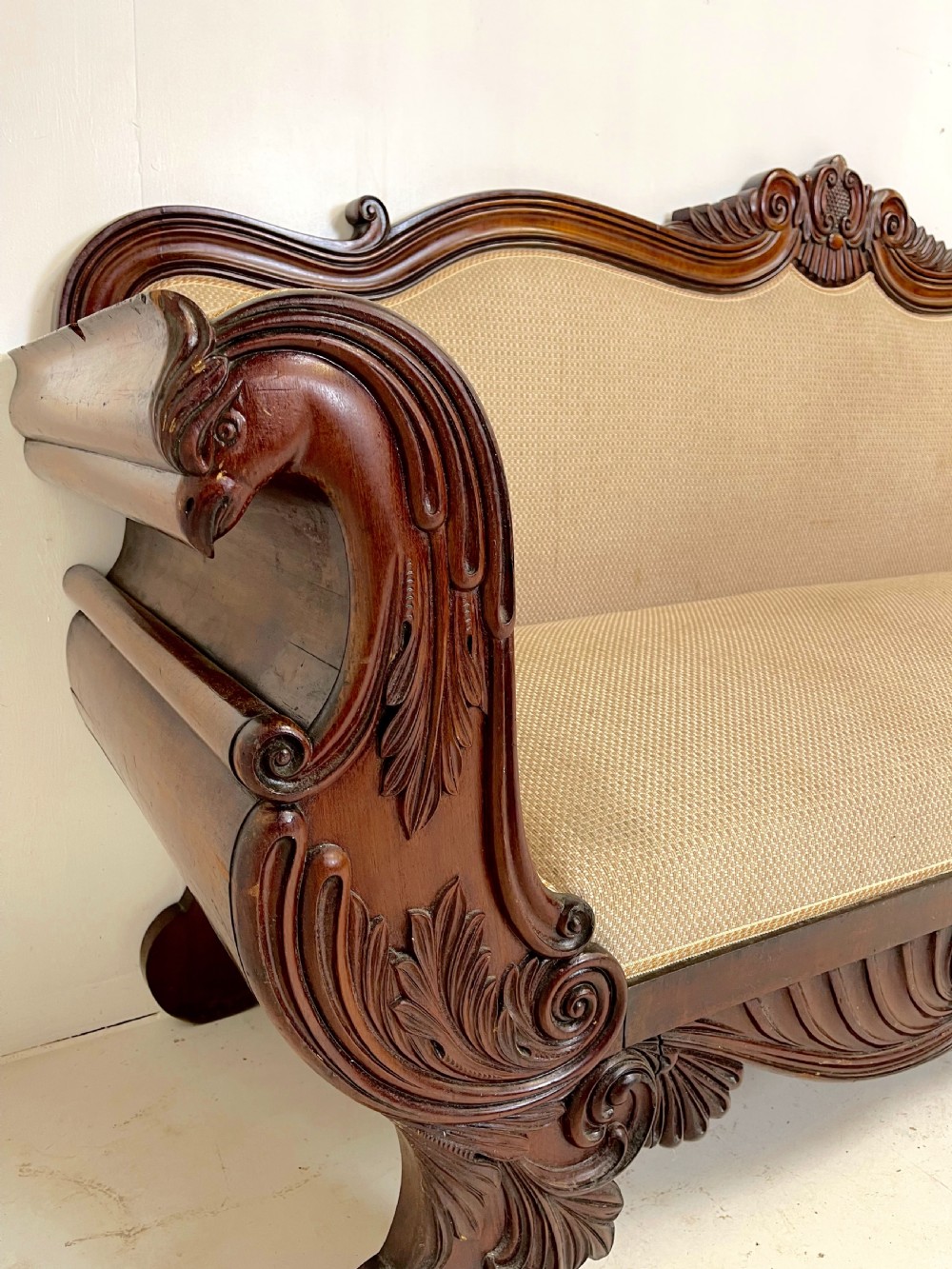 A large antique mahogany sofa featuring intricately hand-carved acanthus scrollwork along the apron and arms, upholstered in a light cream textured fabric. View VI