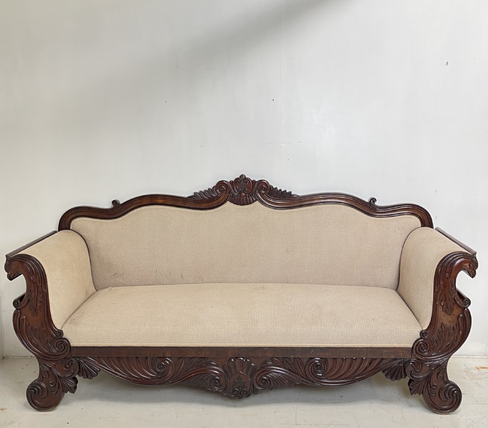 A large antique mahogany sofa featuring intricately hand-carved acanthus scrollwork along the apron and arms, upholstered in a light cream textured fabric. View VII