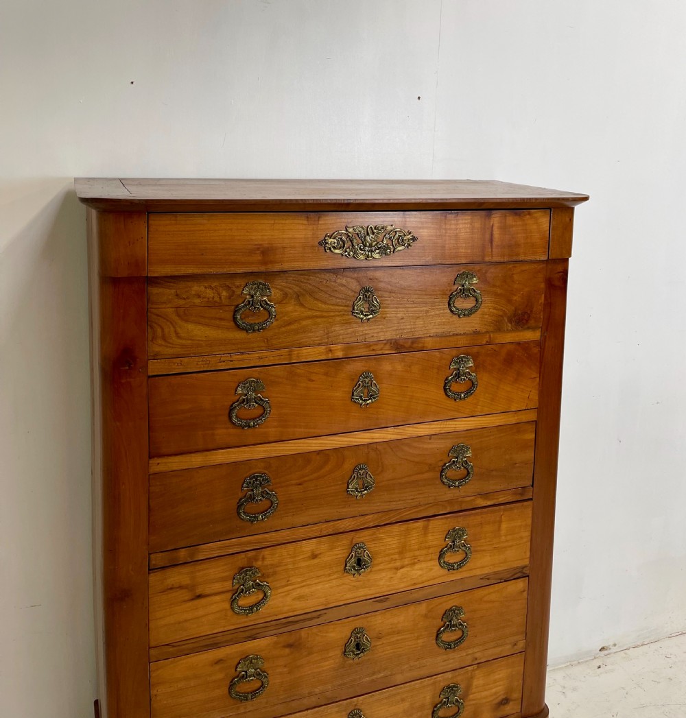 A tall French cherrywood semainier featuring seven drawers with brass drop handles and decorative keyhole escutcheons. View X