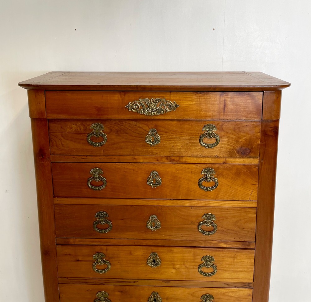 A tall French cherrywood semainier featuring seven drawers with brass drop handles and decorative keyhole escutcheons. View XII