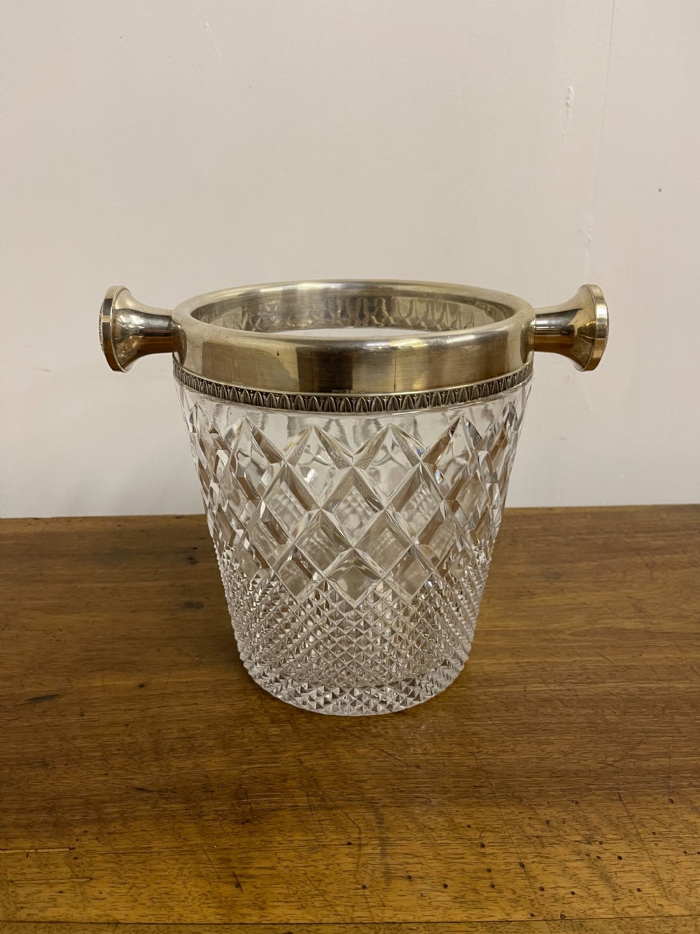 A clear cut glass ice bucket featuring diamond geometric facet patterns with a silver-plated rim and twin side handles. View II