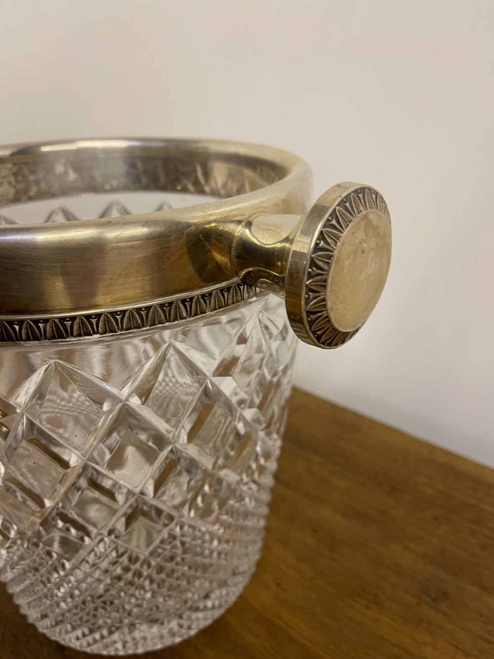 A clear cut glass ice bucket featuring diamond geometric facet patterns with a silver-plated rim and twin side handles. View III