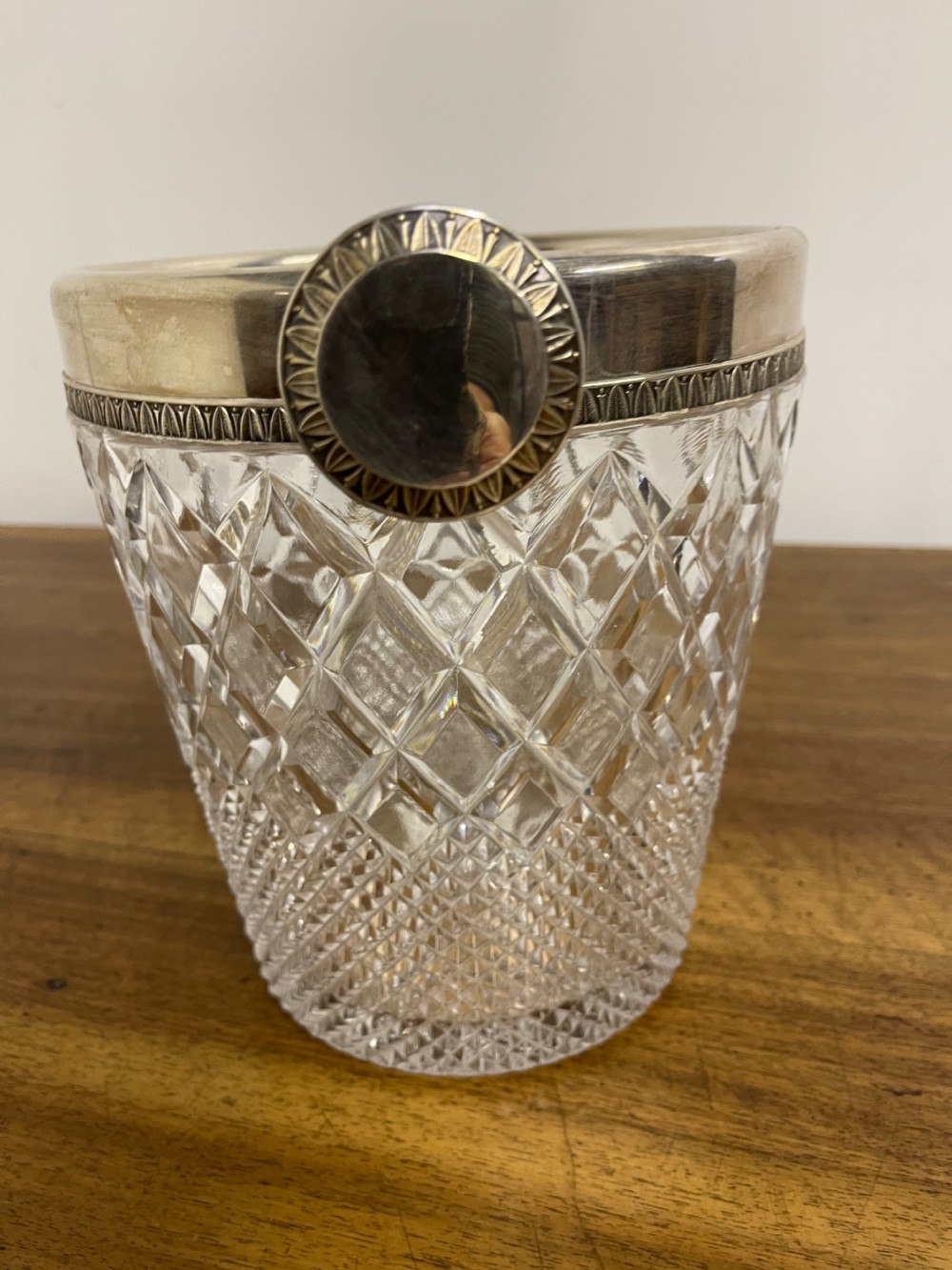 A clear cut glass ice bucket featuring diamond geometric facet patterns with a silver-plated rim and twin side handles. View X