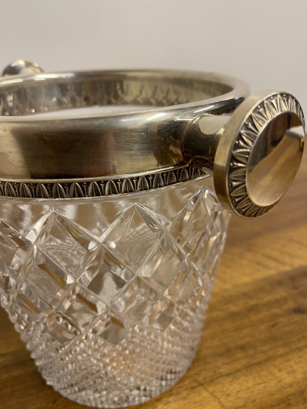 A clear cut glass ice bucket featuring diamond geometric facet patterns with a silver-plated rim and twin side handles. View XII